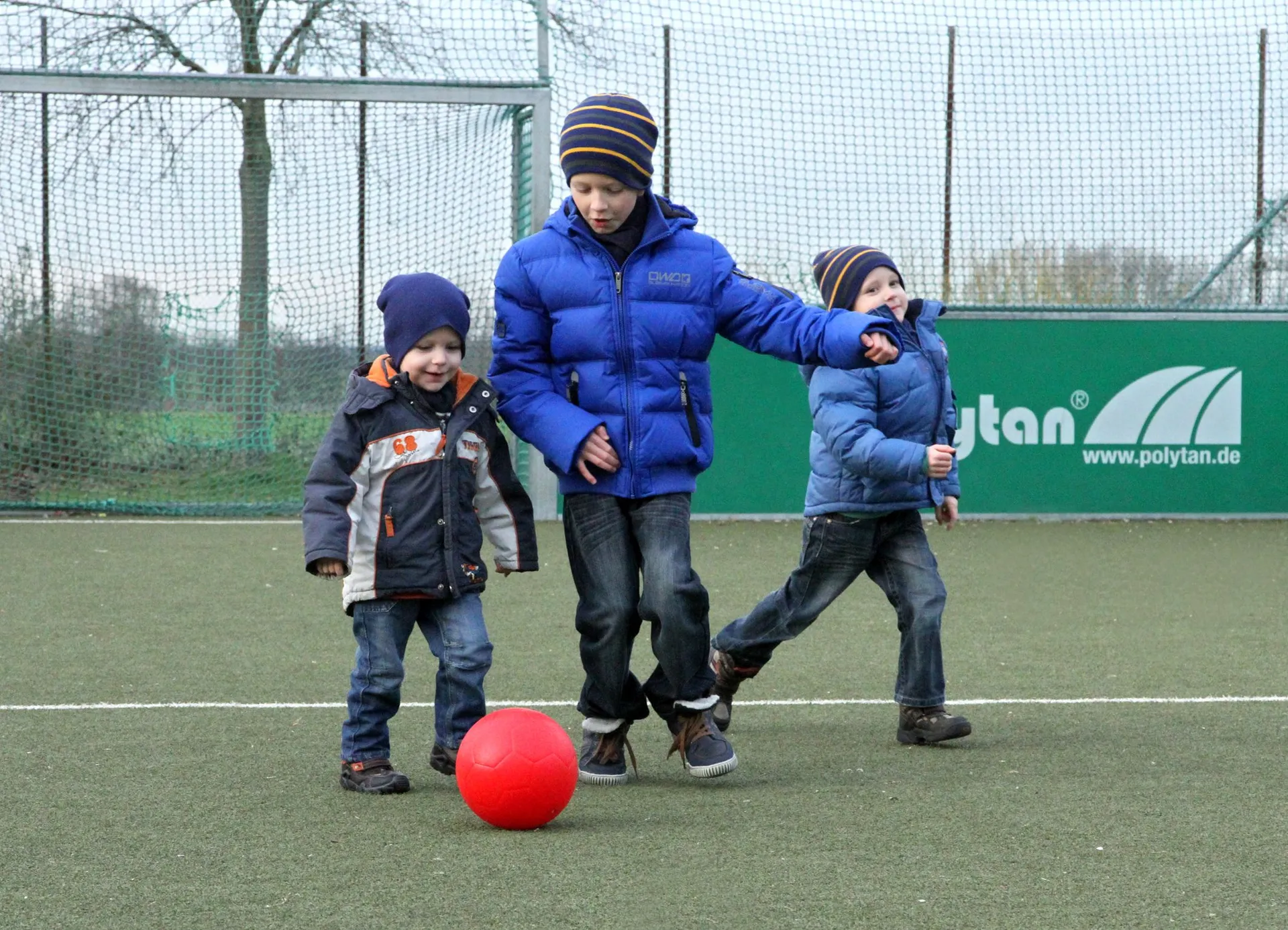 drei Jungen spielen mit einem roten Ball auf einem Soccerplatz
