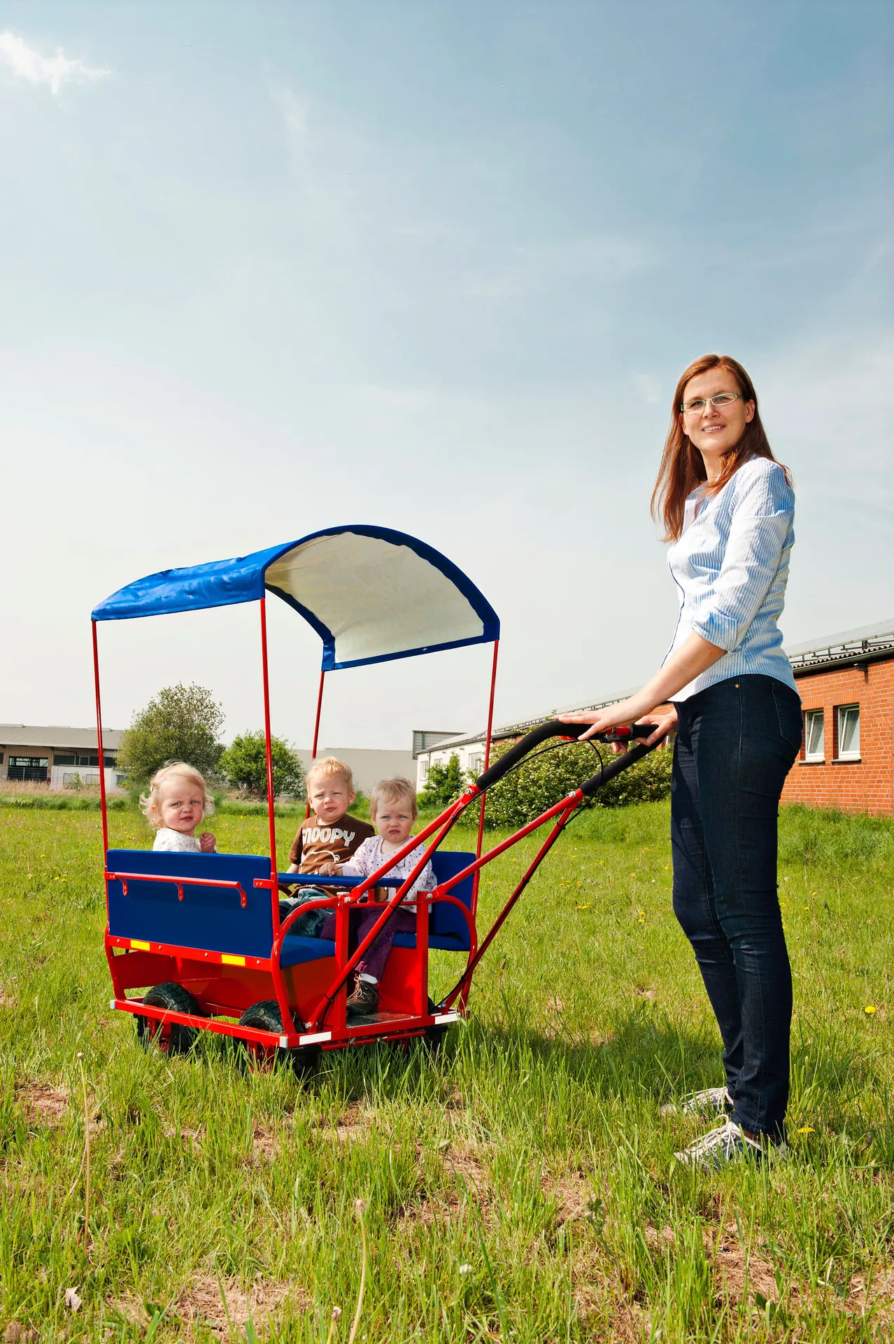 eine Frau mit Krippenwagen und drei Kindern auf einer Wiese